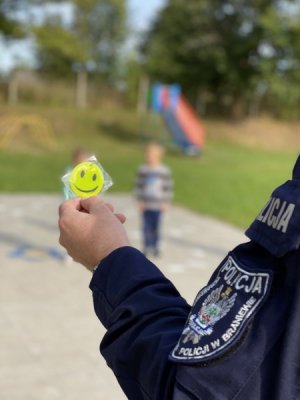 Policjant trzyma w ręku odblask, który za chwilę wręczy każdemu uczniowi